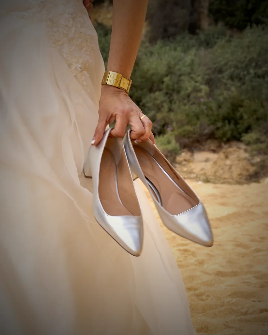 Braut hält ihre silbernen Brautschuhe am Sandstrand in Lagoa an der Algarve