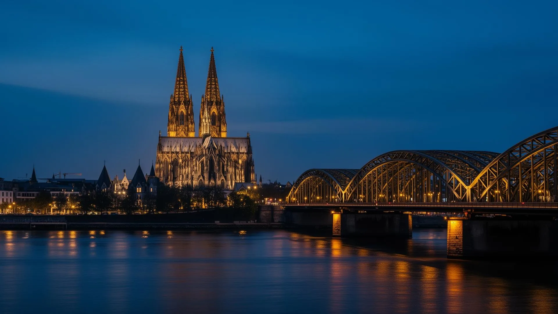 Kölner Dom und Hohenzollernbrücke am Rhein zur blauen Stunde, beleuchtet in warmem Goldton