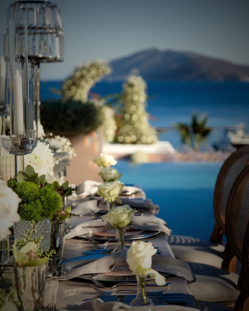 Gedeckte Hochzeitstafel mit weißen Rosen am Meer, im Hintergrund eine Insel