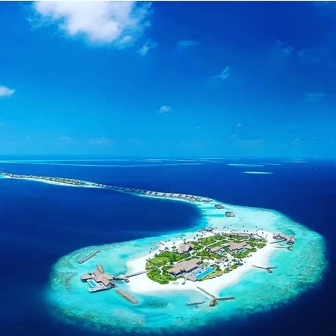 Luftaufnahme einer Resort-Insel auf den Malediven mit Überwasser-Villen und türkisem Lagunenwasser